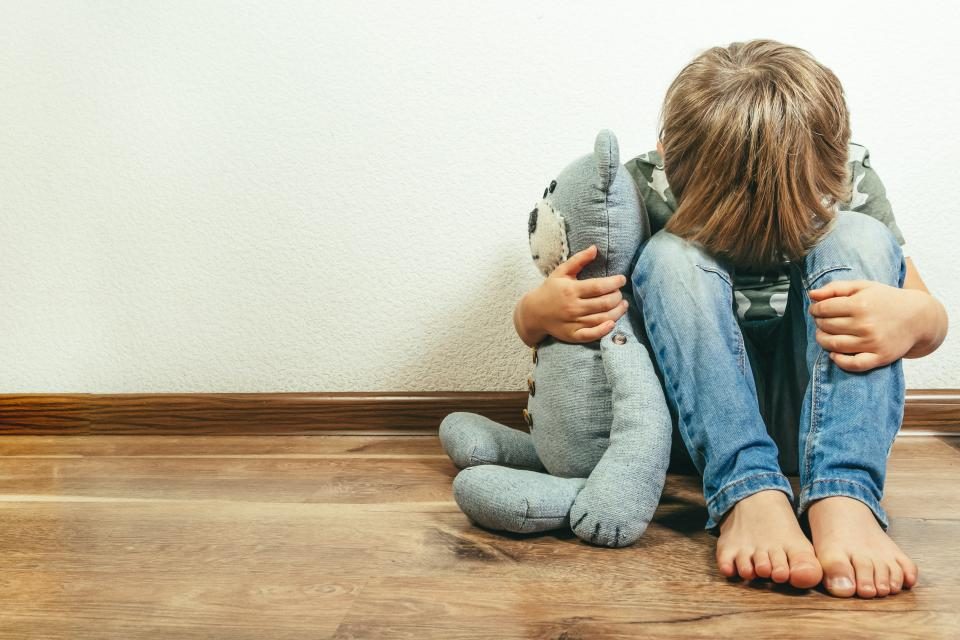 Kind zittend tegen een muur met een knuffelbeer
